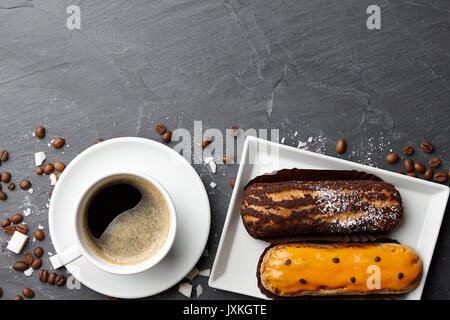 Tazza di caffè con il francese eclairs sulla pietra scura sullo sfondo Foto Stock