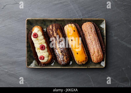 Piastra Rectangulare con differenti eclairs francese su sfondo di pietra, vista dall'alto Foto Stock