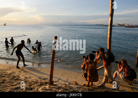 TANZANIA Zanzibar Stone Town, serata al mare, turistico con telecamere di balneazione snaping youngster / TANZANIA Insel Sansibar, Stonetown, abends am Meer, Touristen fotgrafieren badende Jugendliche Foto Stock