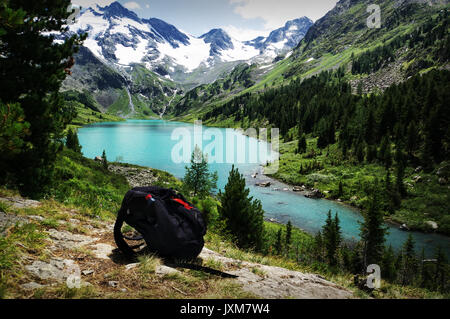 Zaino nero giacente sulla pietra contro un paesaggio di montagna con il turchese del lago. Il concetto di escursionismo nel selvaggio. Foto Stock