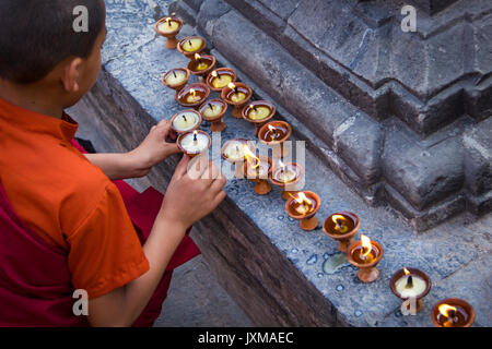 Giovane monaco buddista illuminazione di lampade a burro a Swayambhunath Stupa, noto anche come il Tempio delle Scimmie, a Kathmandu, Nepal. Foto Stock