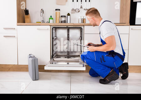 Repairman seduta vicino lavastoviglie iscritto negli appunti in cucina Foto Stock