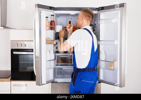 Tecnico di maschio rotto Riparazione Apparecchio frigorifero con il cacciavite Foto Stock