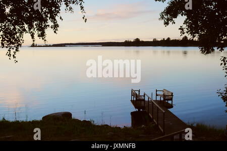 Un pontile riflessa nell'acqua ancora al tramonto, wet orme sul pontile dopo una serata nuotare Foto Stock