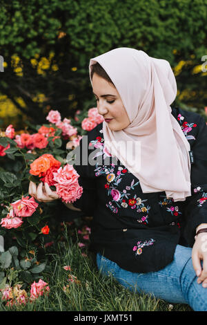 Giovane donna indossa hijab ammirando fiori Foto Stock