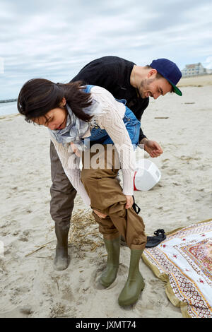 Giovane mare pesca matura mettendo su waders sulla spiaggia Foto Stock