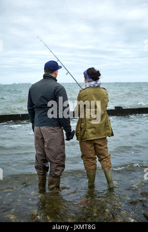 Vista posteriore del giovane uomo profondo della caviglia in acqua insegnamento ragazza pesca in mare Foto Stock