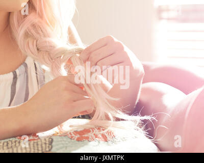 Giovane donna capelli da intreccio, femmina amico giacente sul letto accanto a lei, close-up, metà sezione Foto Stock