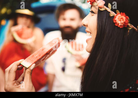 Giovane donna boho mangiare fette di melone al festival Foto Stock