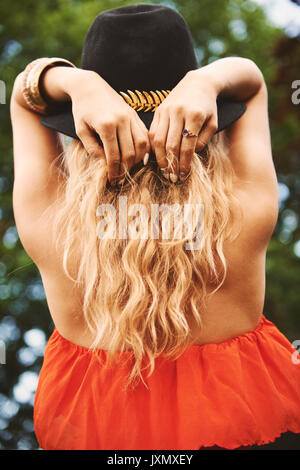 Vista posteriore del giovane donna boho in trilby con le mani dietro la testa al festival Foto Stock