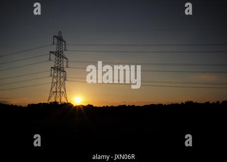 Il sole tramonta accanto ad un pilone dell'lasciando la torre stagliano contro un cielo arancione Foto Stock