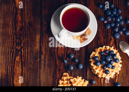 White tazza di tè con mirtillo e waffles fatti in casa su sfondo di legno. Copia spazio sulla sinistra. Foto Stock