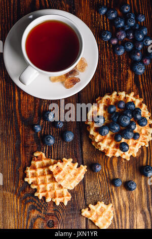 White tazza di tè con mirtilli e tutto rotto e waffles Belgi su sfondo di legno. Orientamento verticale. Foto Stock