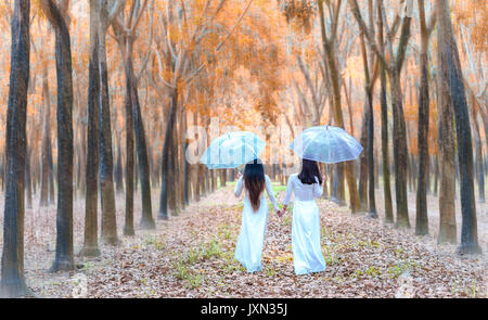 Ragazza vietnamita in tradizionali abiti lunghi o Ao Dai holding ombrello tunica andare verso la fine della strada nel bosco su una soleggiata giornata estiva in Dong Nai, Vietnam Foto Stock