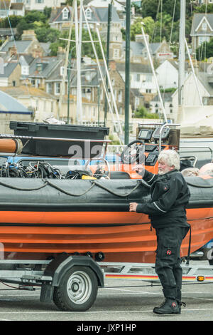 Un uomo anziano in una muta, accanto a una barca rigida gonfiabile (nervatura) su un rimorchio, in Penzance Harbour, Cornwall, Inghilterra, Regno Unito. Foto Stock