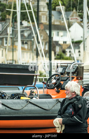 Un uomo anziano in una muta, accanto a una barca rigida gonfiabile (nervatura) su un rimorchio, in Penzance Harbour, Cornwall, Inghilterra, Regno Unito. Foto Stock