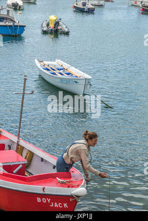 Una donna di mezza età in una piccola imbarcazione a motore, nel processo di ormeggio nel porto di Penzance, Cornwall, Inghilterra, Regno Unito. Foto Stock