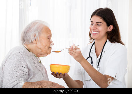 Felice medico donna zuppa di alimentazione con cucchiaio a Senior paziente in ospedale Foto Stock