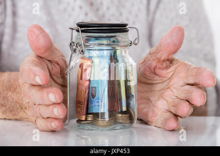 Close-up di Senior donna Protezione mano il vasetto di vetro di denaro Foto Stock