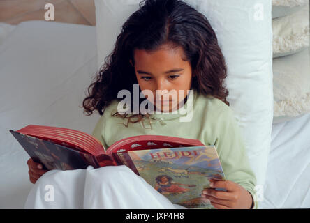 Giovane bambina 7-10 anni storybook di lettura a letto americano africano/Caucasian Foto Stock