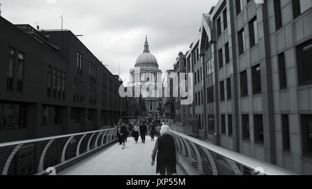 Fotografia in bianco e nero di persone che attraversano il Millenium Bridge, nei pressi della Cattedrale di St Paul, in un giorno nuvoloso a Londra. Foto Stock