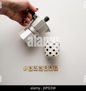 Moka italiana macchina per caffè con un nero bianco punteggiato mug e la scrittura #domenica fatta con scrabble le lettere. Formato quadrato. Foto Stock