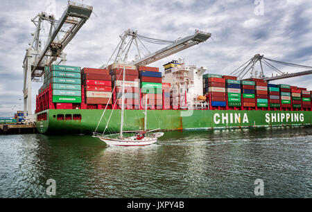 OAKLAND, CA-MAR 9, 2014: il porto di Oakland a Oakland, in California. Una barca a vela passa da un caricato nave cargo, mostra la scala. Foto Stock