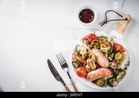 Barbecue. Assortimento di varie carni alla brace salsicce, con verdure per barbecue - funghi, pomodori, zucchine, cipolle. Su marmo bianco tabella, sulla piastra, w Foto Stock