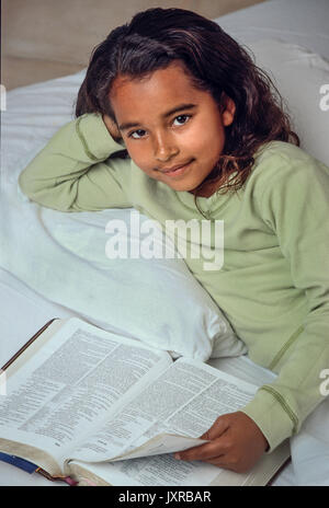 Ragazza giovane 7-10 anno di età bambino leggendo la Bibbia nel letto americano africano/Caucasian elevato angolo dal di sopra Myrleen Pearson Foto Stock