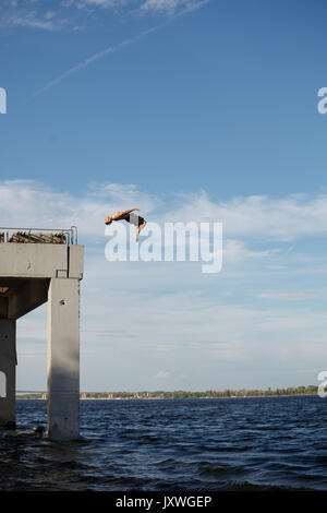 Un uomo è il salto in mare da un molo di alta. Adrenalina e sport estremi. Torna capriola in salto. Foto Stock