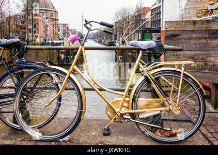 Oro bike appoggiata contro la ringhiera di protezione su un canale ad Amsterdam Foto Stock