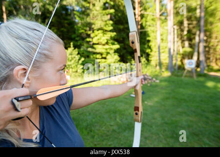 Arciere femmina di puntamento a freccia sulla scheda Target nella foresta Foto Stock