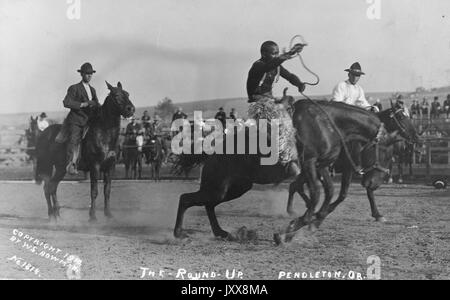 Cowboy a cavallo in una area di rodeo, con gli spettatori e gli altri partecipanti in background, in corrispondenza del primo annuale Pendleton round-up, 1910. Foto Stock