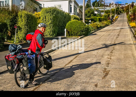 Ciclista femmina tenta di ciclo in salita al Baldwin Street - la strada più ripida del mondo, Dunedin, Nuova Zelanda Foto Stock