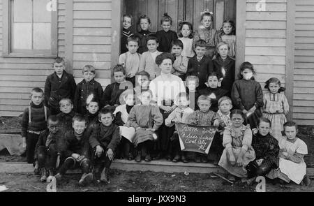 Foto di paesaggio a lunghezza intera di scolari seduti fuori dell'edificio, uno studente afroamericano in basso a sinistra, 1920. Foto Stock