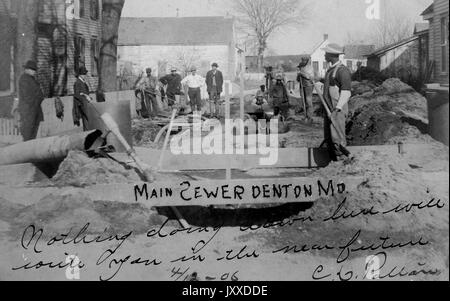 Un gruppo di lavoratori americani con espressioni neutre si trova all'esterno con strumenti e attrezzature, lavorando sul sistema fognario di una città americana, probabilmente Denton, Maryland, 1915. Foto Stock