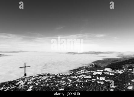 Una croce di legno in cima del Monte Subasio, con un mare di nebbia al di sotto e la città di Assisi (Umbria) in background Foto Stock