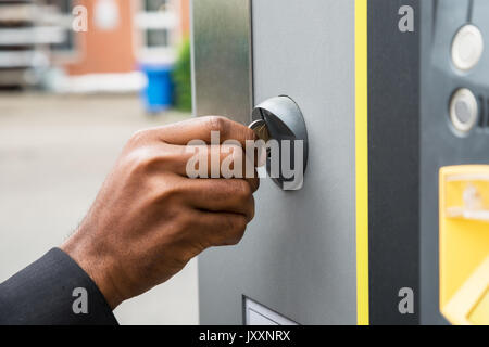 Close-up di persona la mano inserimento di moneta nel parcometro Foto Stock