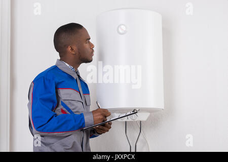 I giovani africani idraulico maschio Holding Appunti Guardando Boiler elettrico Foto Stock