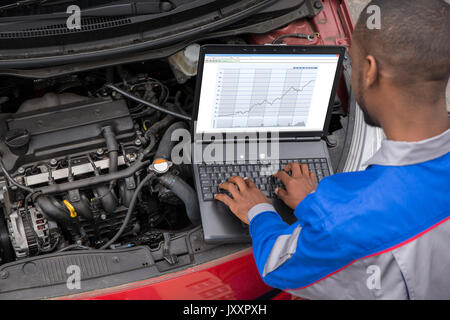 Giovane Maschio meccanico tramite computer portatile mentre esaminando auto motore Foto Stock