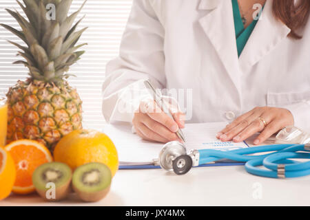 Nutrizionista scrivere i record medici e ricette con frutta fresca Foto Stock