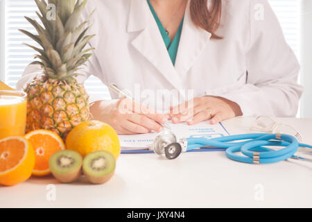Nutrizionista scrivere i record medici e ricette con frutta fresca Foto Stock