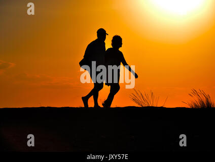 Sagome di persone che stanno camminando al tramonto Foto Stock