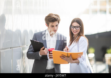 Business man in tuta con tablet e caffè nelle mani di parlare con business donna su notebook di piallatura circa. Foto Stock