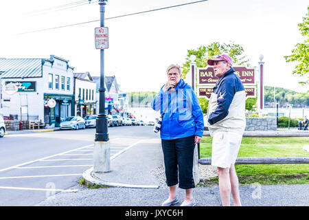 Bar Harbor, Stati Uniti d'America - 8 Giugno 2017: coppia Senior in piedi sul marciapiede da oceanfront resort inn segno con lungomare nel centro di villaggio in estate Foto Stock