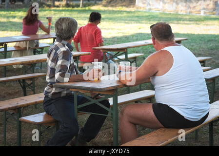 Due uomini seduti su un banco a bere birra al festival Foto Stock