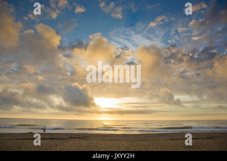 Distante uomo a camminare sulla spiaggia al tramonto Foto Stock