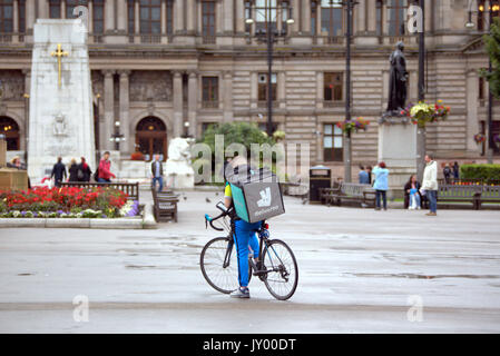 Wet George Square Glasgow giovane ragazzo consegna bike ciclista Deliveroo Consegna del cibo scrivere messaggi in attesa per il lavoro offrendo al di fuori sulla strada Foto Stock