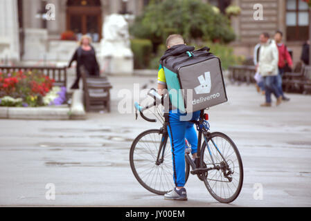 Wet George Square Glasgow giovane ragazzo consegna bike ciclista Deliveroo Consegna del cibo scrivere messaggi in attesa per il lavoro offrendo al di fuori sulla strada Foto Stock