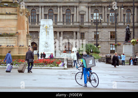 Wet George Square Glasgow giovane ragazzo consegna bike ciclista Deliveroo Consegna del cibo scrivere messaggi in attesa per il lavoro offrendo al di fuori sulla strada Foto Stock